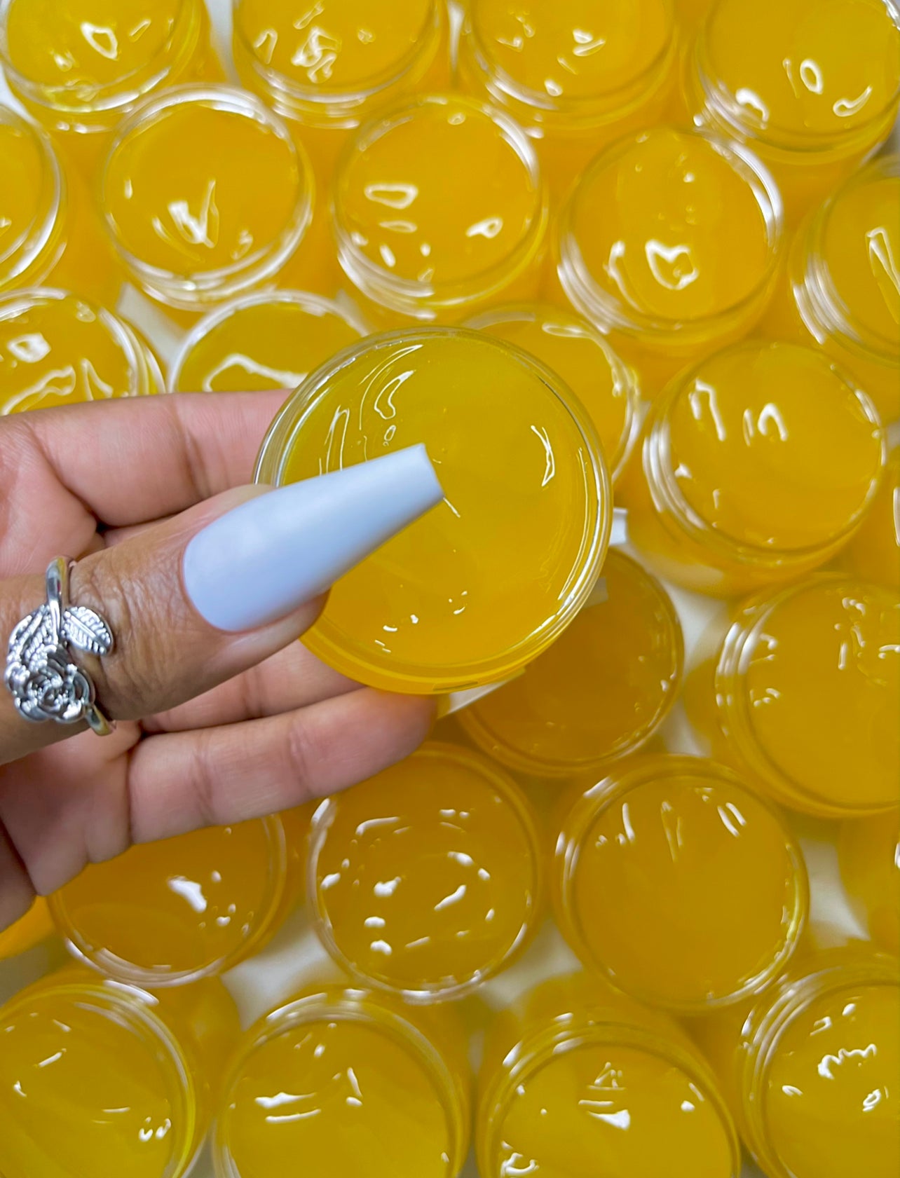 A person's hand holding a jar of yellow-colored leveling jelly serum, with a close-up on the jar showing a dime-size application.