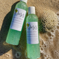 2 light blue shower gels laying on sand by the beach with bubbles 