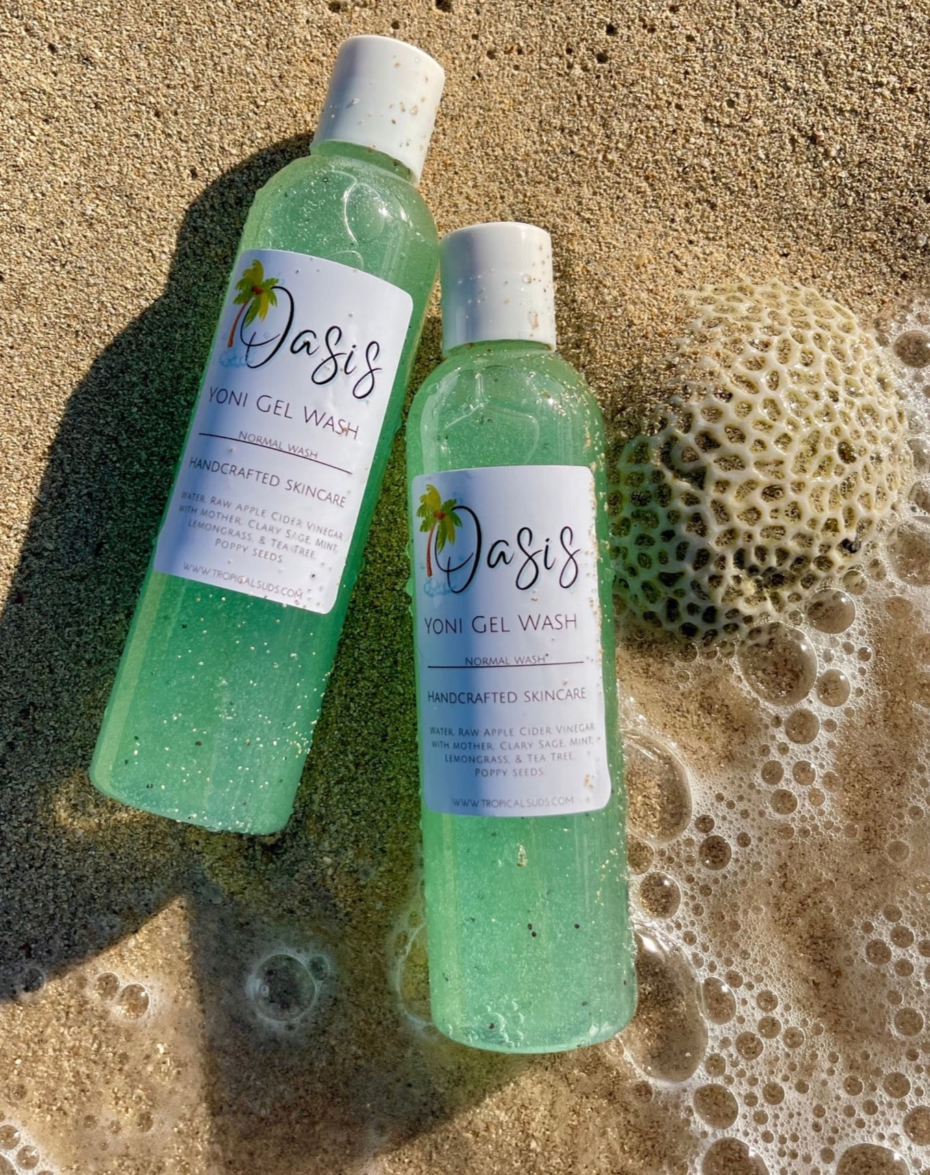 2 light blue shower gels laying on sand by the beach with bubbles 