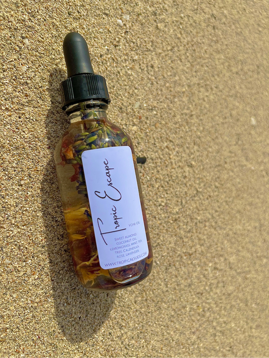 A clear glass bottle with a dropper filled with yellowish liquid, filled with the Tropic Escape Oil, placed on a sandy surface.